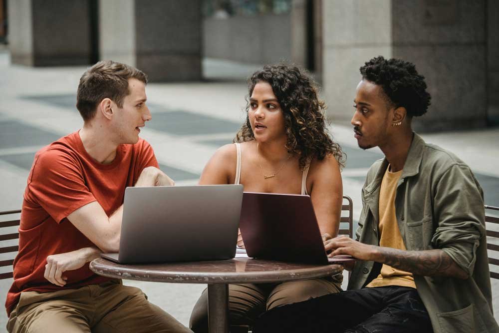 Three colleagues talking at a table with their laptops